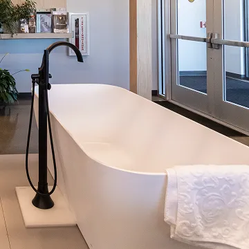 Freestanding white bathtub with black floor-mounted faucet and towel draped over the rim at The Water Closet.