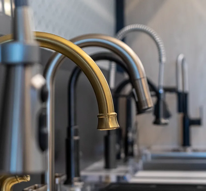 Row of kitchen faucets in matte black, brass, and stainless finishes on a white countertop display.