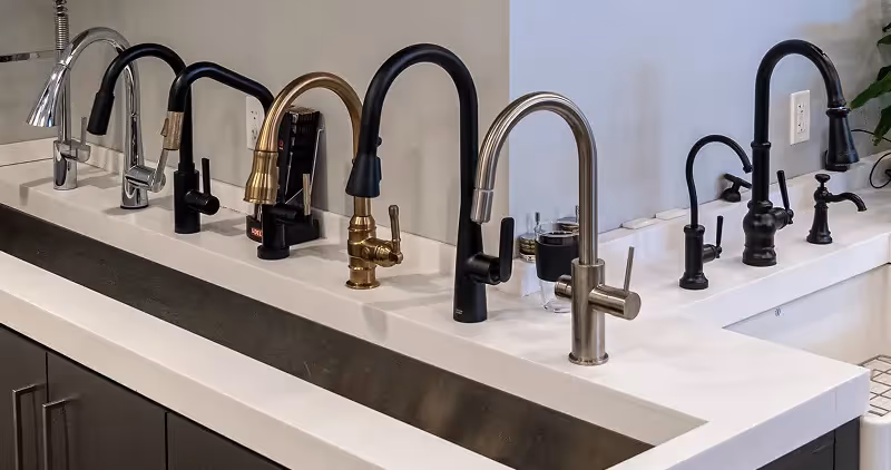 Wall display of modern kitchen and bath faucets in various finishes at The Water Closet showroom.