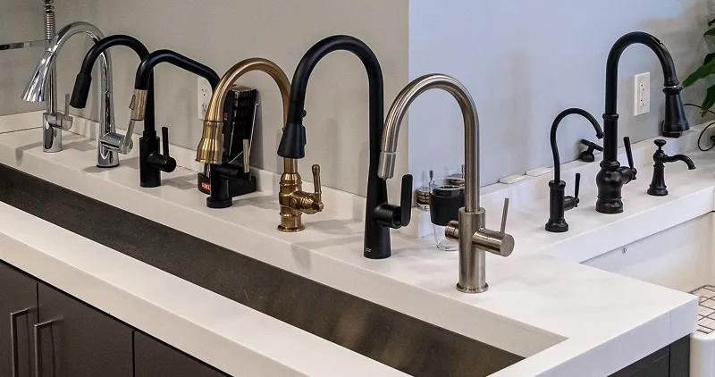 Wall display of modern kitchen and bath faucets in various finishes at The Water Closet showroom.