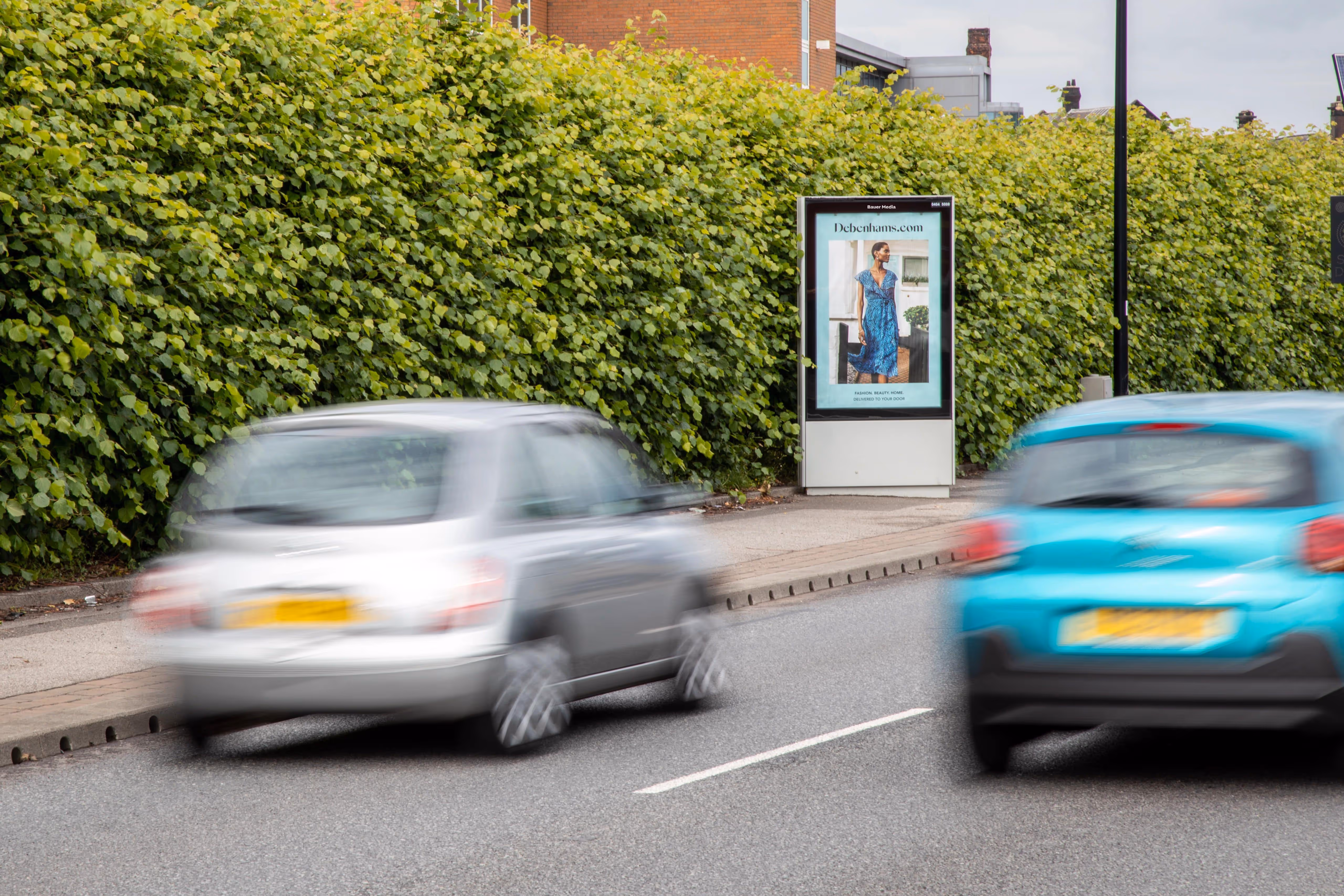 Debenham's light blue with a womans blue dress Adshel advertisement surrounded by 2 cars