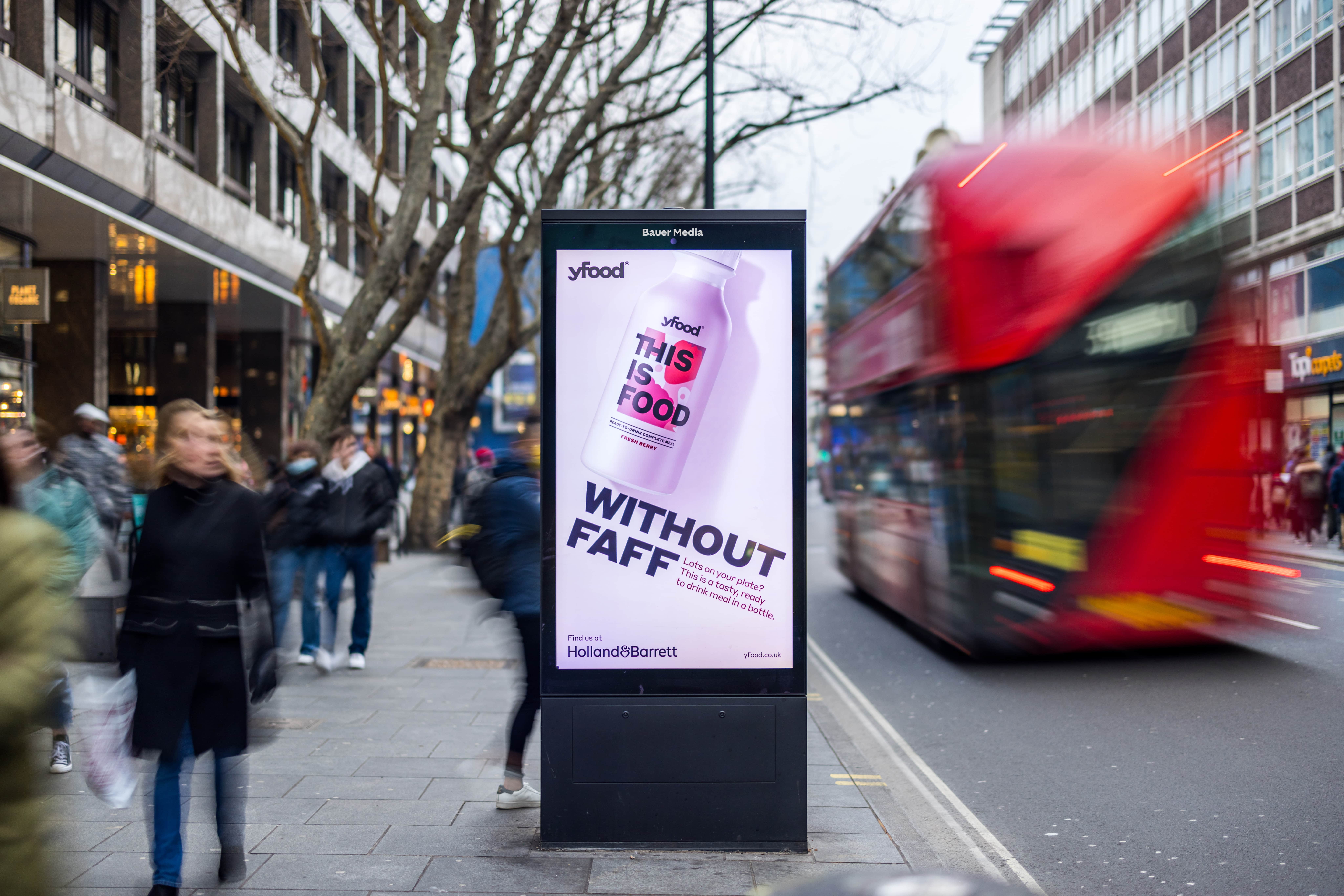 Yfood's pink 'Without faff' Adshel Live advertisement on a London high street with lots of shoppers
