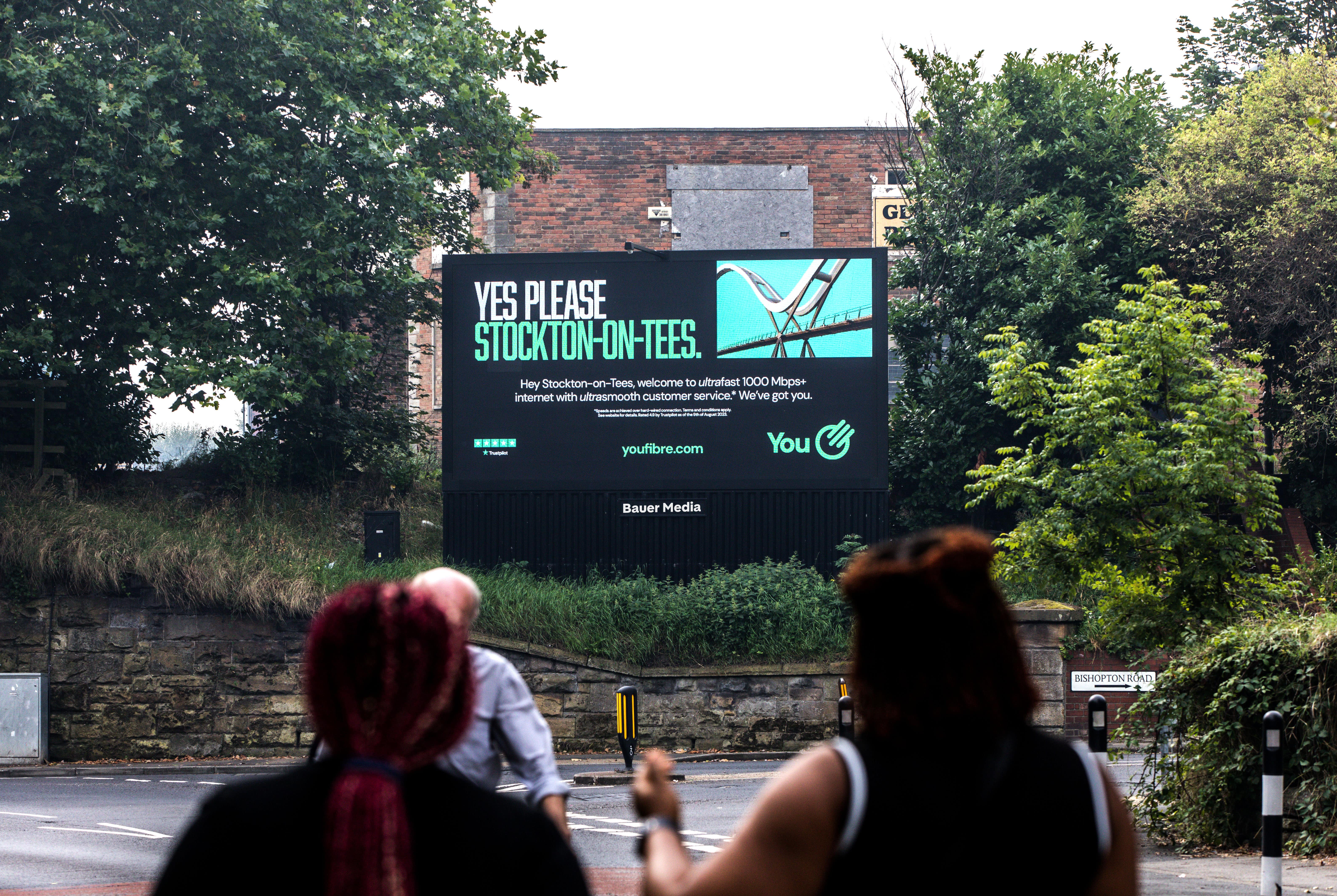 A large digital billboard advertisement surrounded by trees and greenery