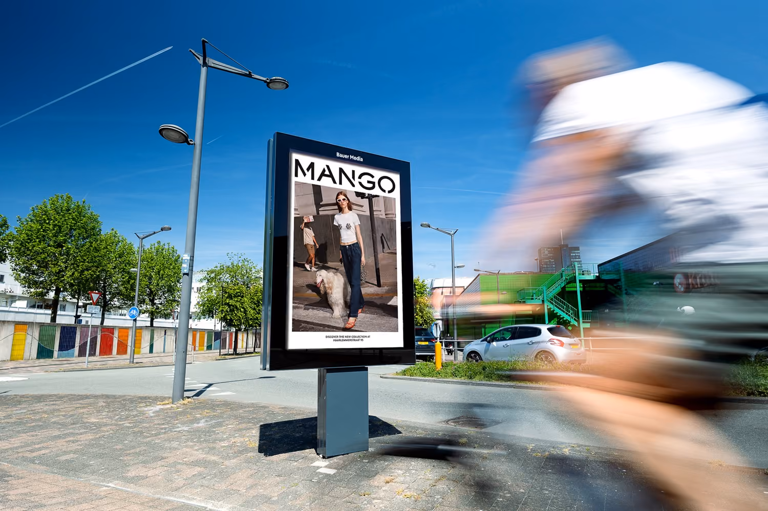 Advertentiebord langs een straat met een Mango-reclame, op de voorgrond een wazige fietser in beweging.