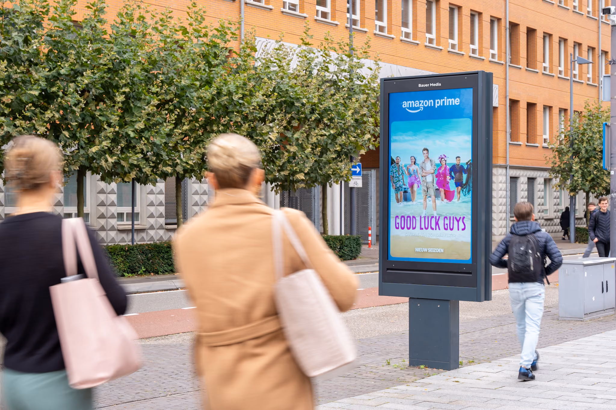 Reclamebord op straat met een Amazon Prime advertentie voor de serie Good Luck Guys, met daarvoor lopende mensen.