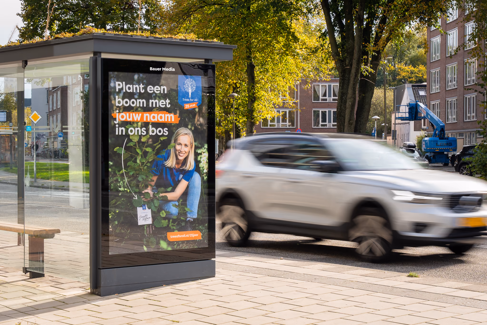 Abri met advertentie waarin een vrouw een jonge boom vasthoudt en de tekst promoot om een boom met jouw naam te planten.