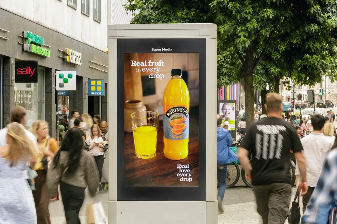 A Robinsons advert on a digital outdoor poster screen, plus lots of people on a busy high street.