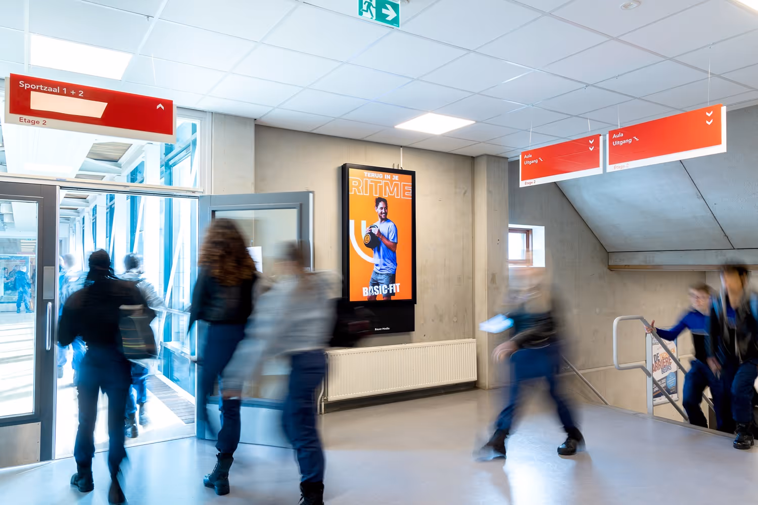 Digitaal scherm in hal van school met scholieren die voorbij lopen