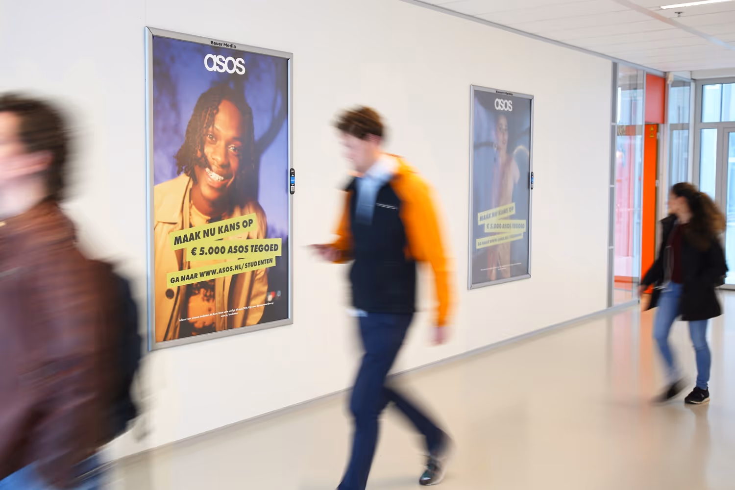 2 reclameobjecten aan muur in hal van school met scholieren die voorbij lopen