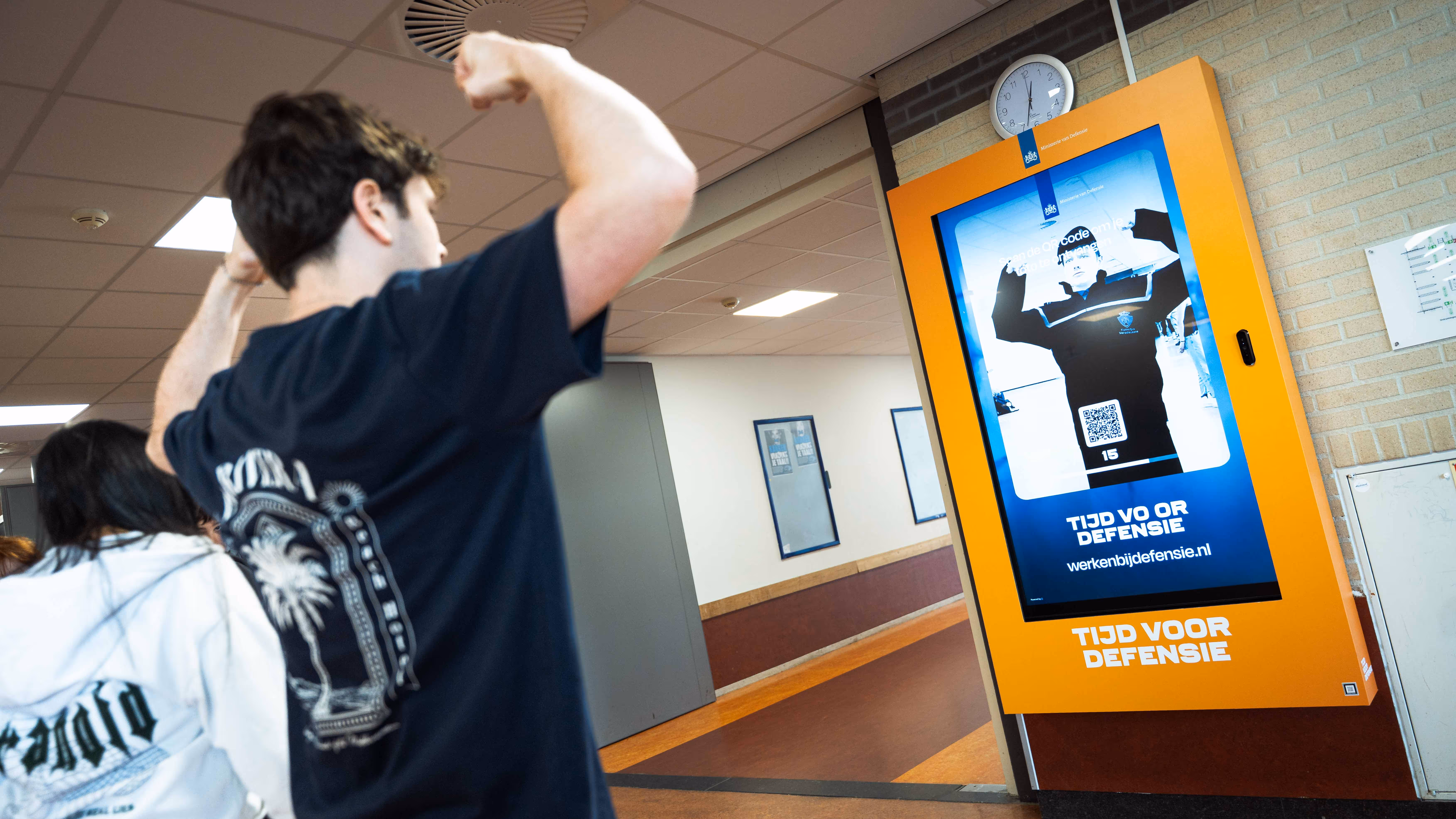 Jongen staat voor digitaal scherm met daarop een reclame van Defensie