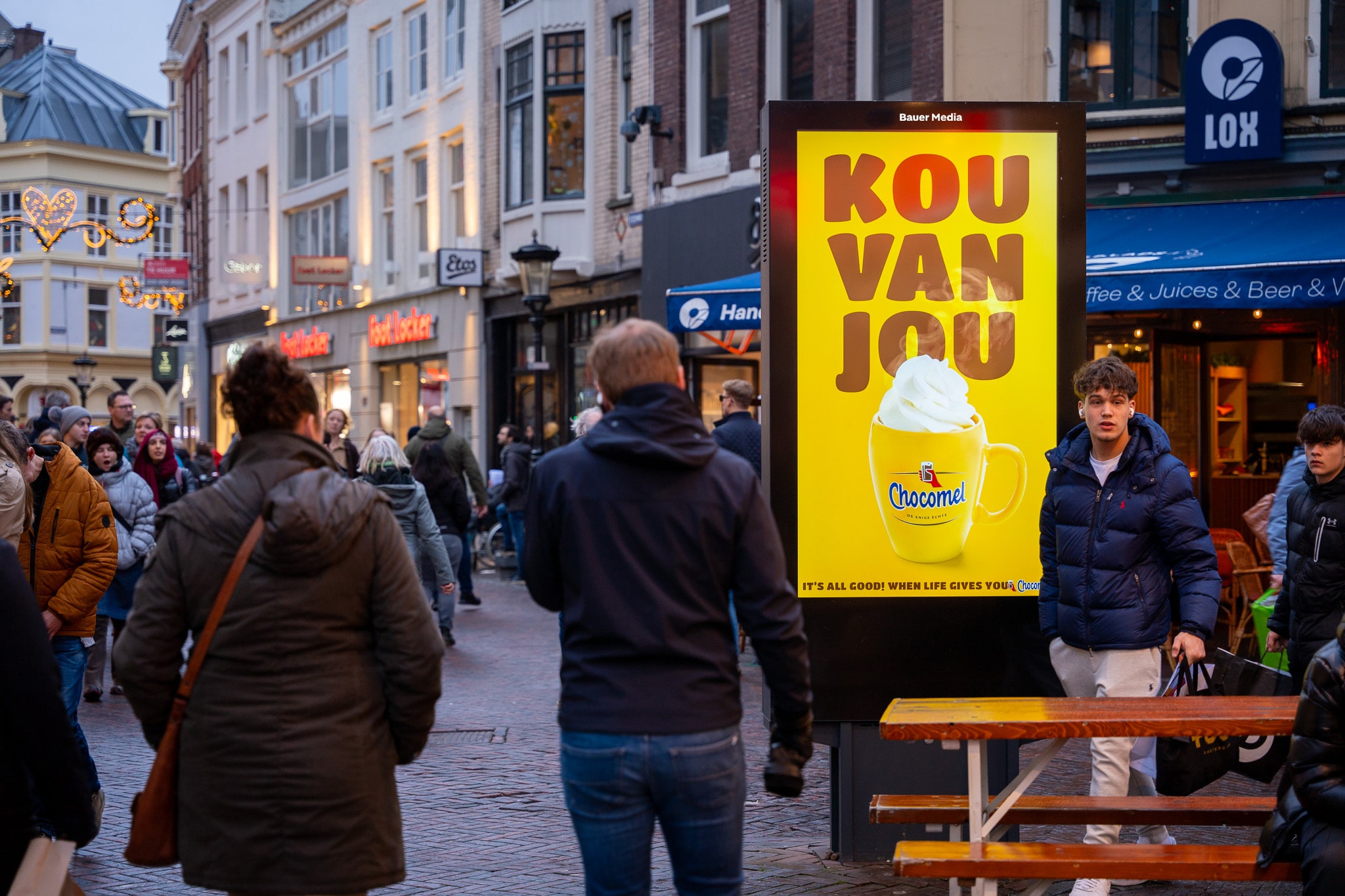 Digitaal scherm met Chocomel reclame in winkelstraat met voorbijgangers