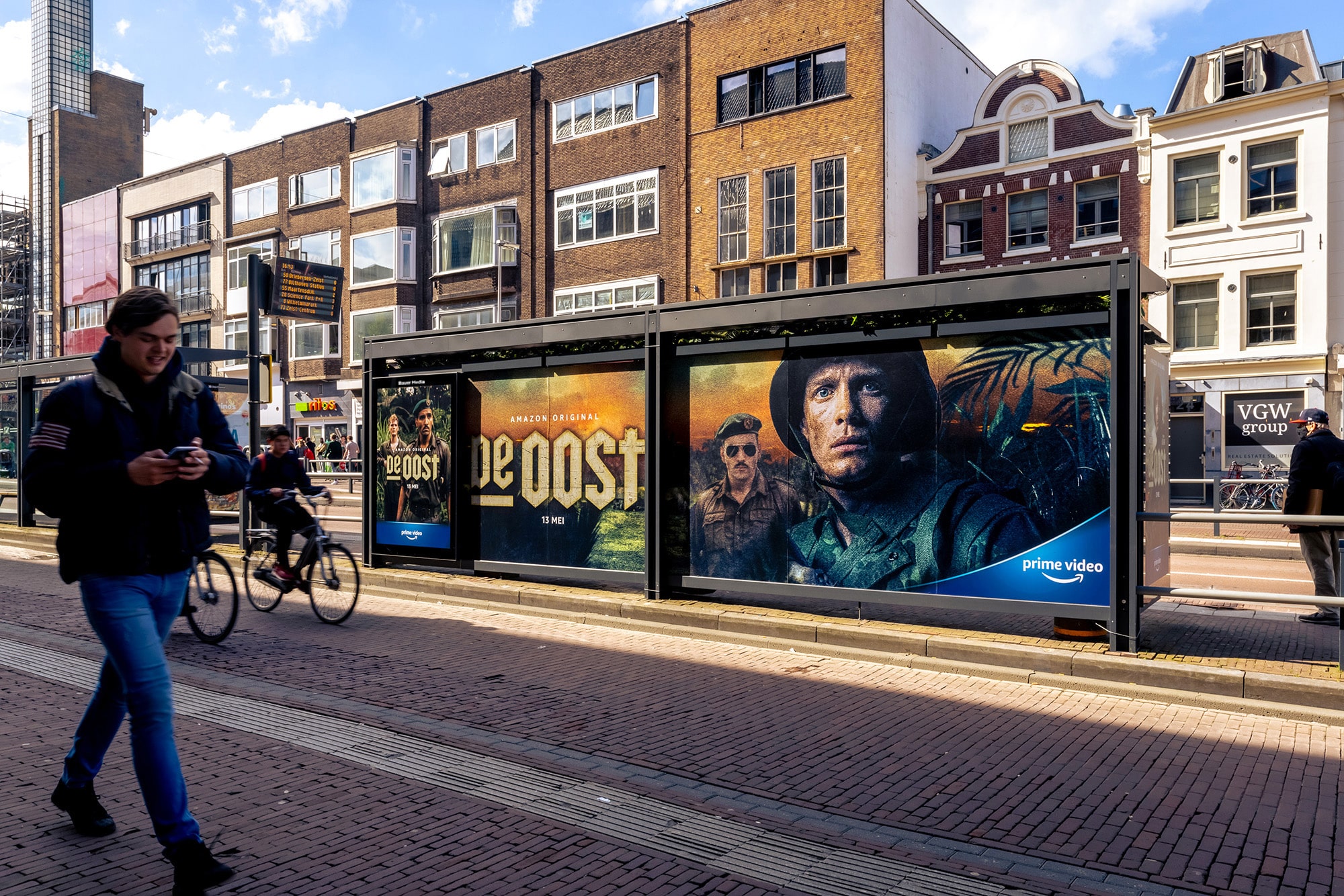 Bushalte met reclame van De Oost en man loopt voorbij