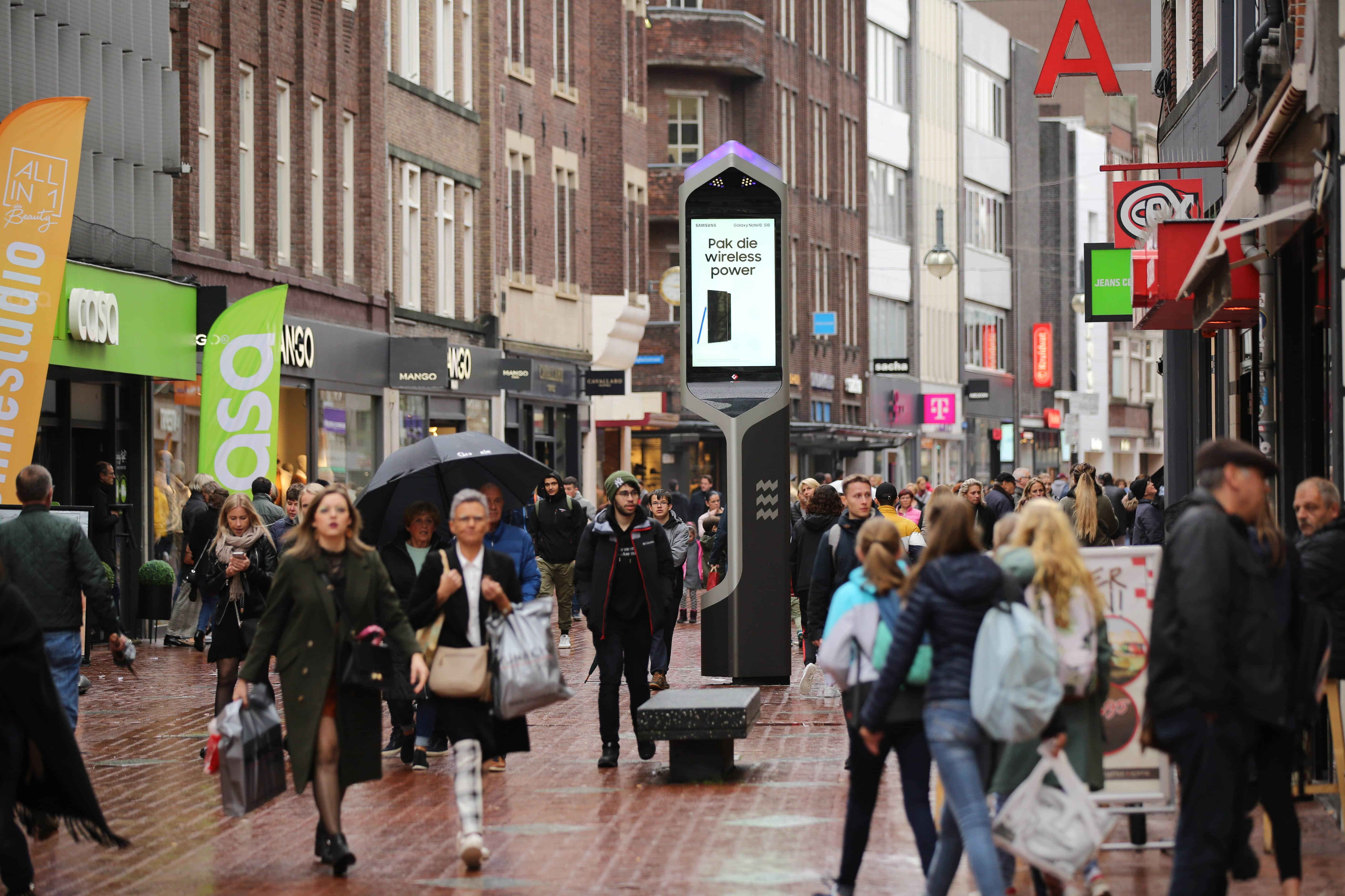 Digitaal reclameobject in drukke winkelstraat met veel winkelend publiek