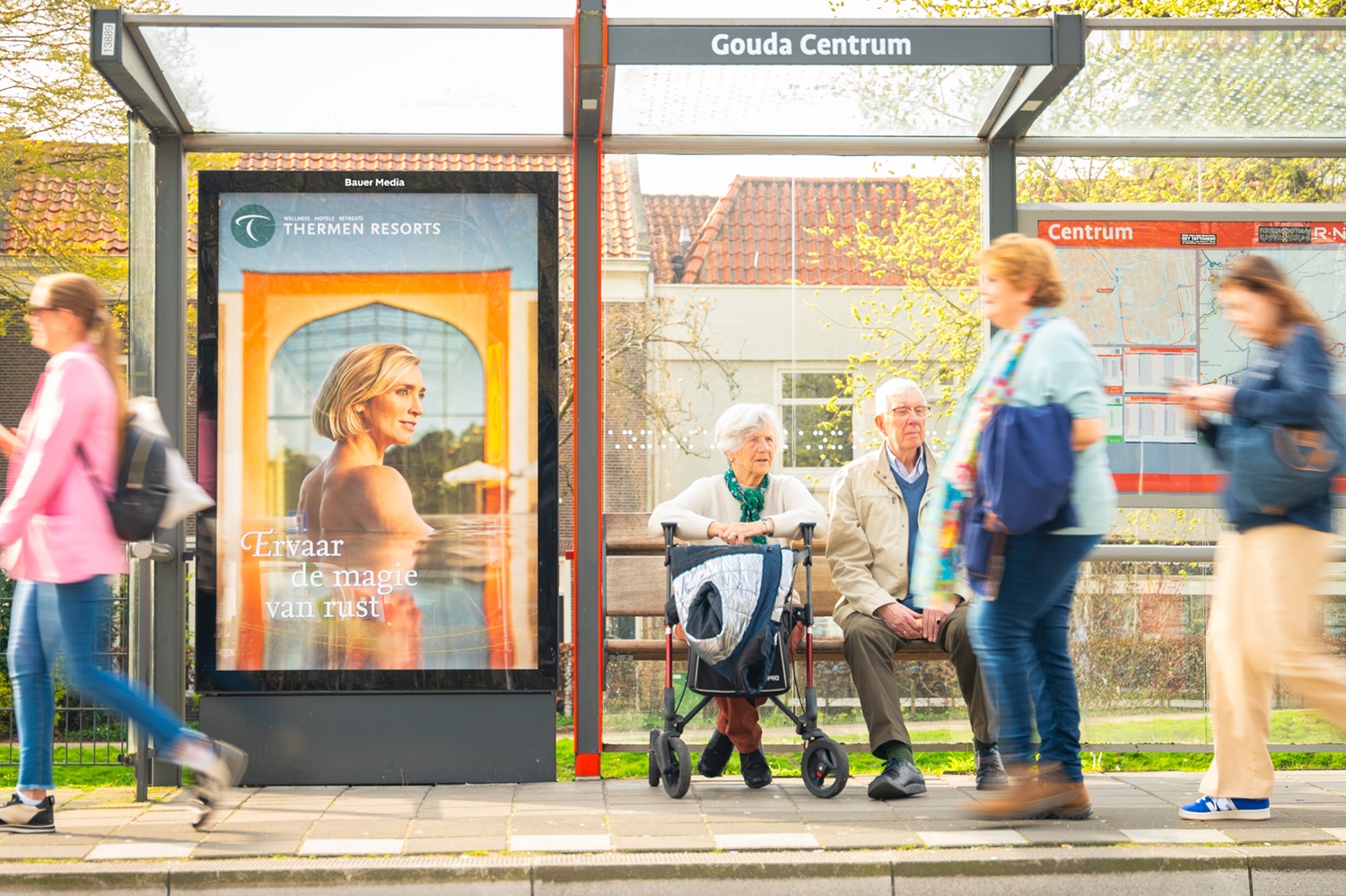Bushalte in Gouda met wellness reclame en wachtende mensen