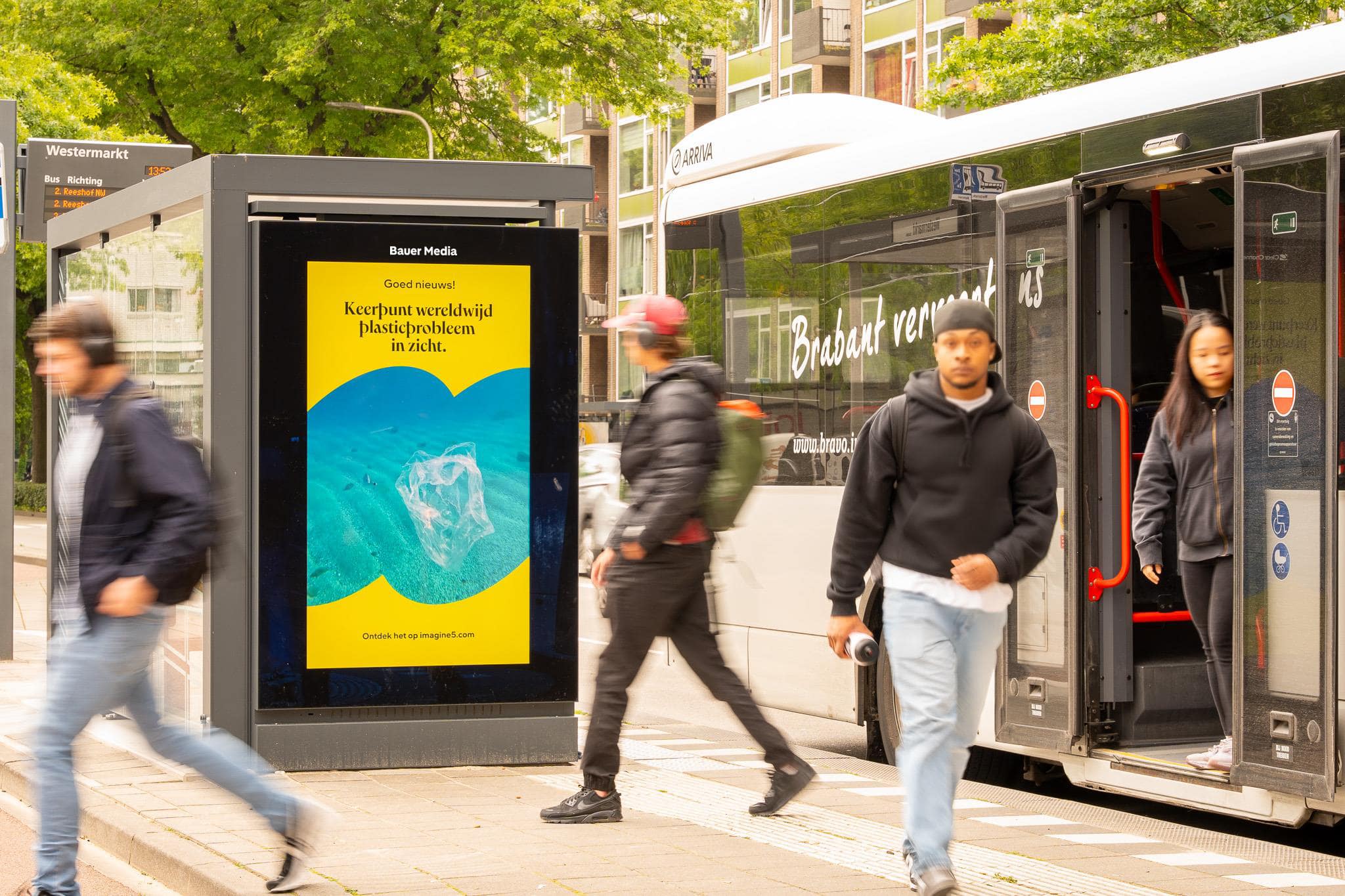 Bushalte met campagne van Imagine5 en 4 personen stappen uit bus. 