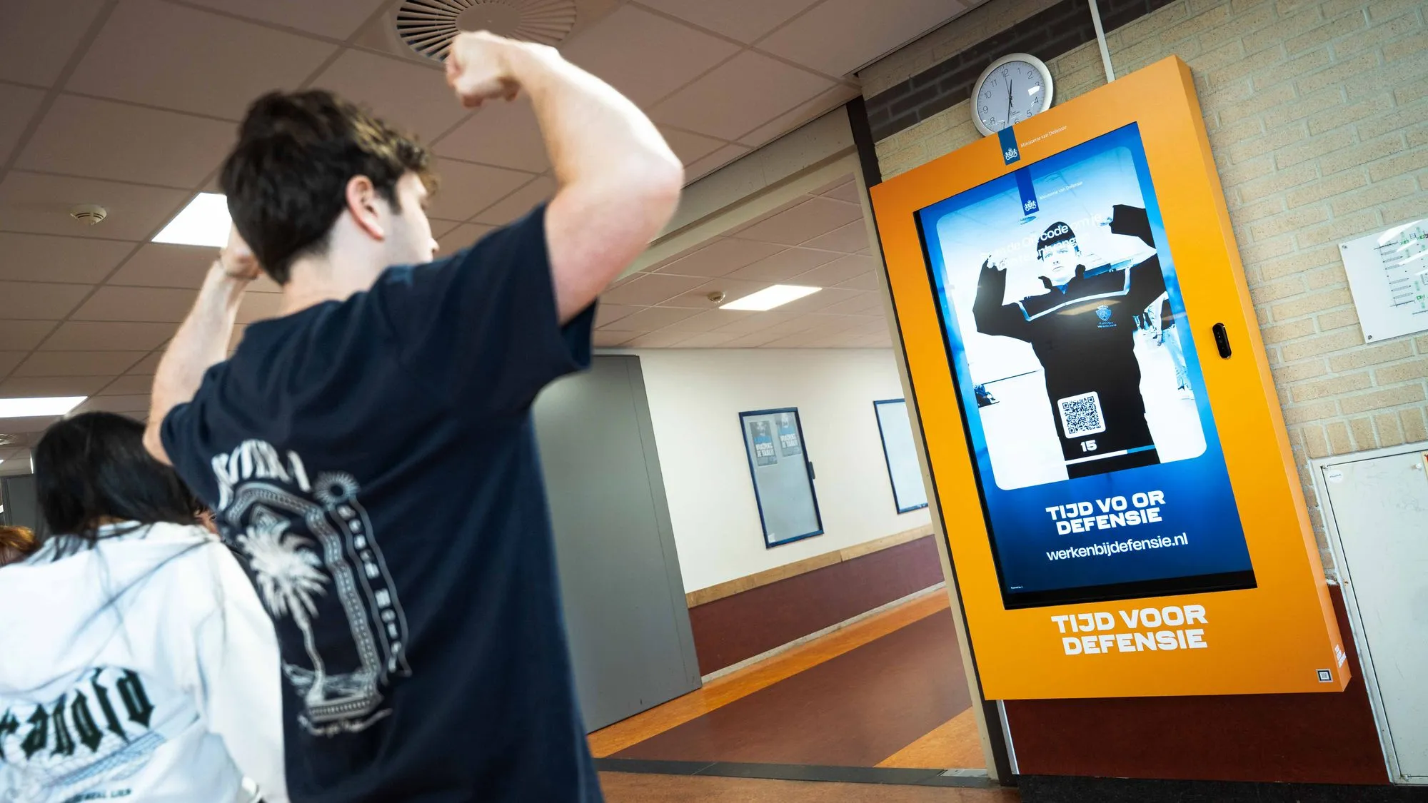 Jongen staat voor digitaal scherm met daarop een reclame van Defensie