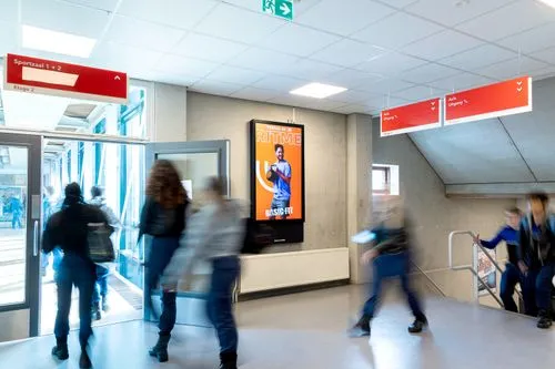 Digitaal scherm in hal van school met scholieren die voorbij lopen