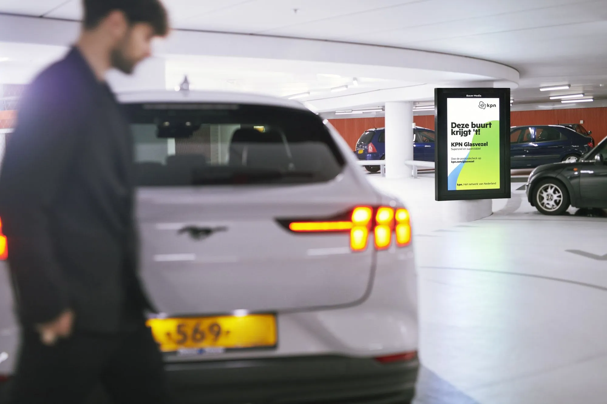 Man loopt voorbij auto in parkeergarage met op de achtergrond een digitaal scherm met reclame