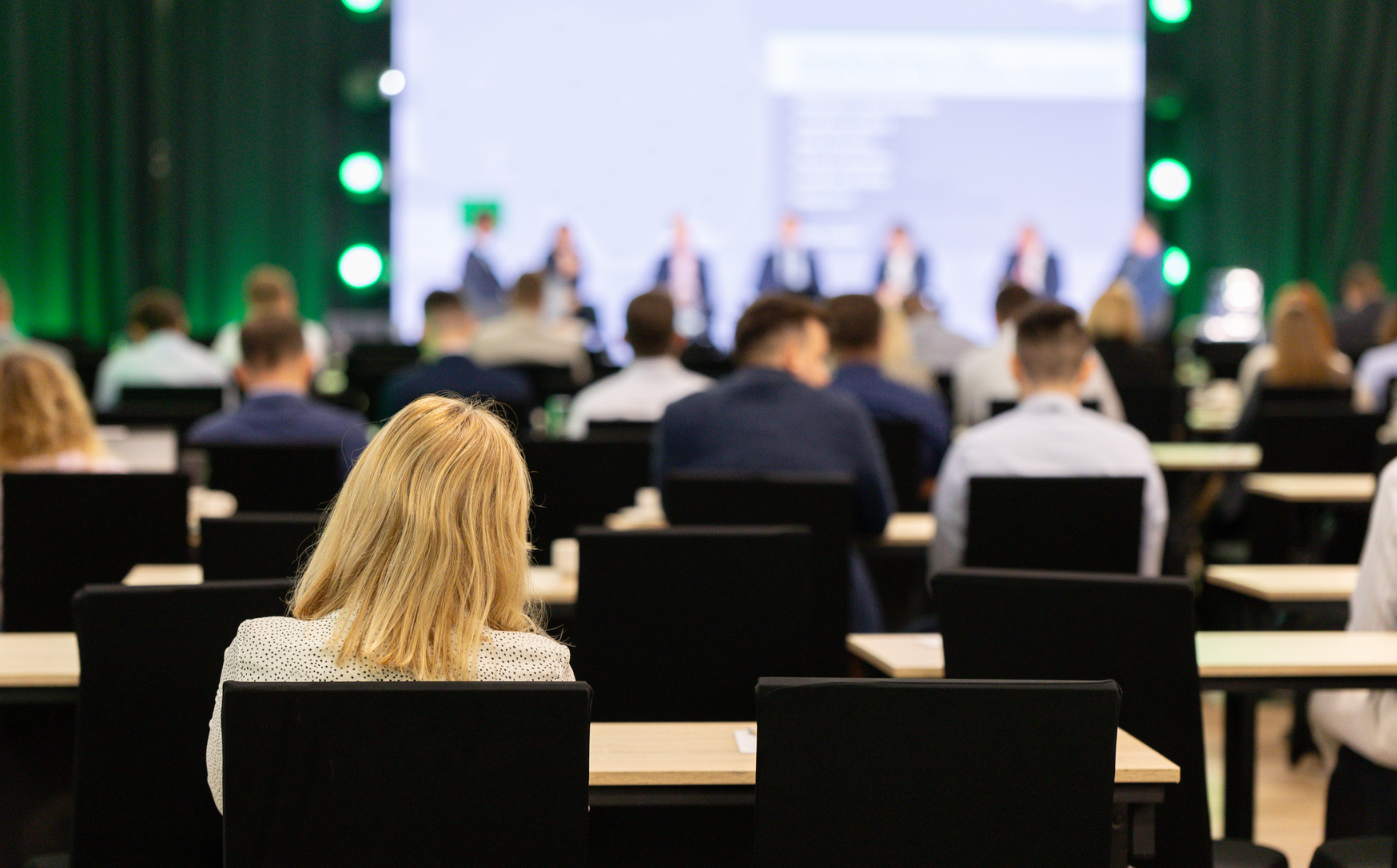 Audience seated at a corporate conference facing a speaker panel on stage