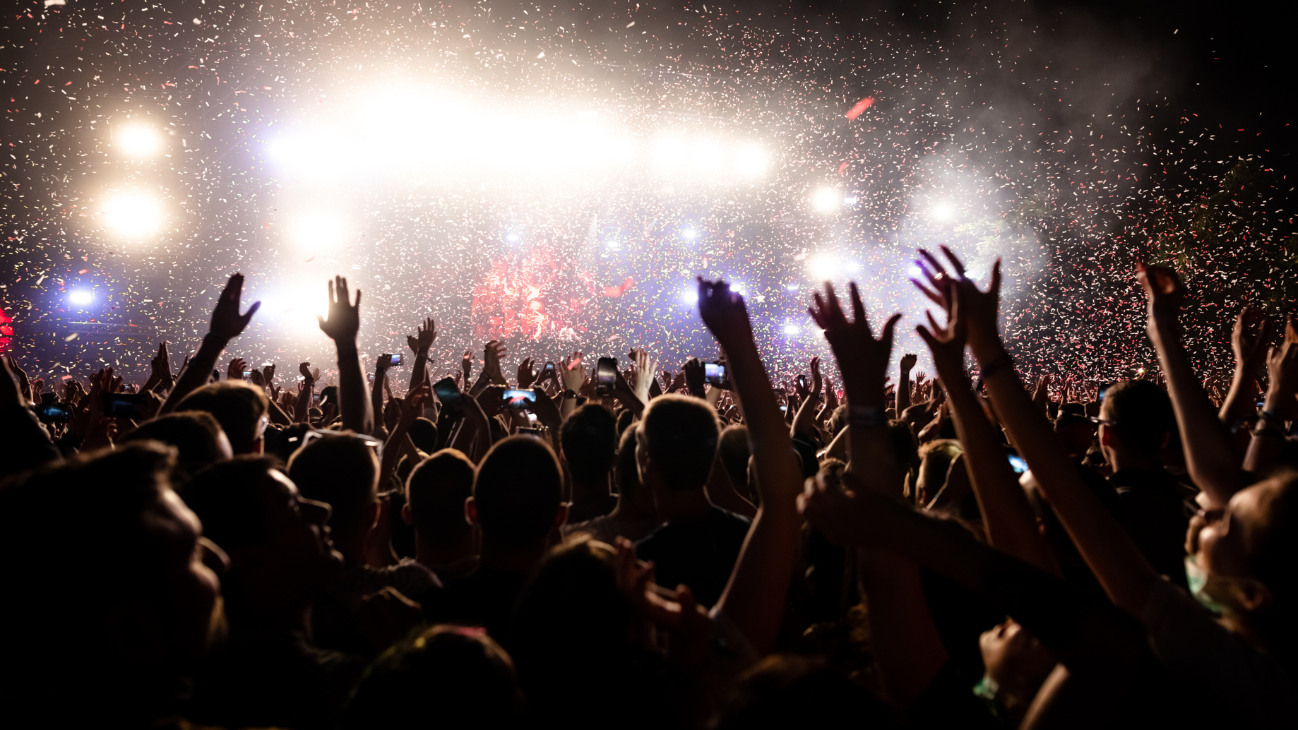 Crowd with raised hands under confetti and stage lights at a live performance