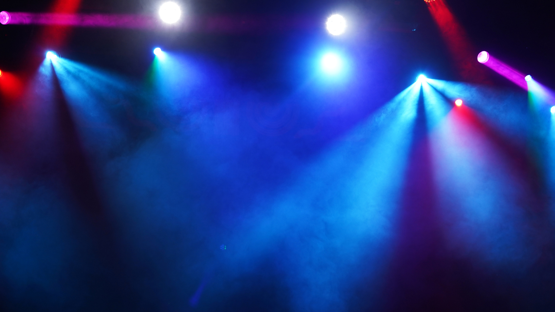 Blue and magenta stage lights sweeping through haze above a live production