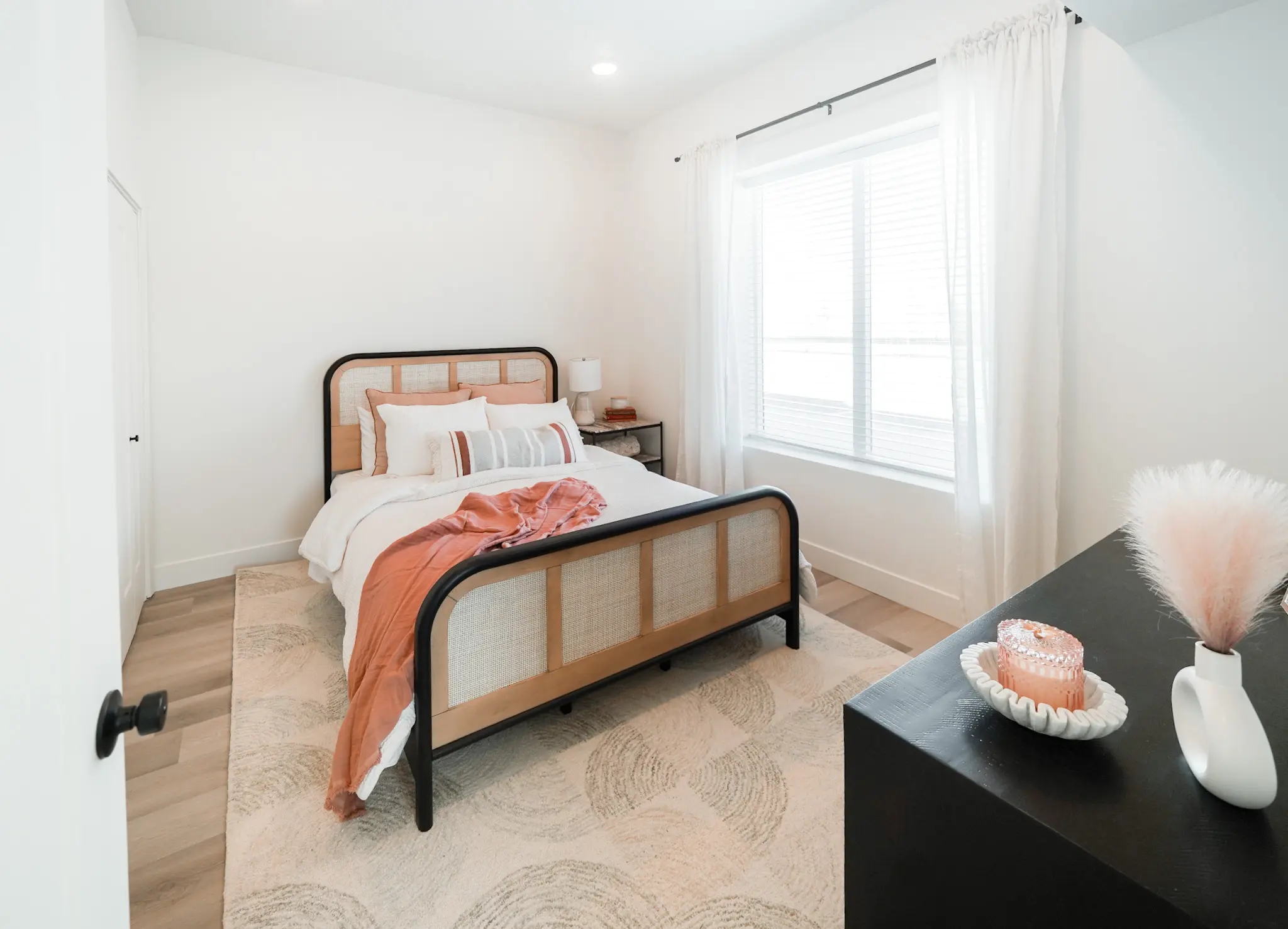 A bedroom with a single bed with a pink blanket and white comforter. There is a candle on the black dresser.