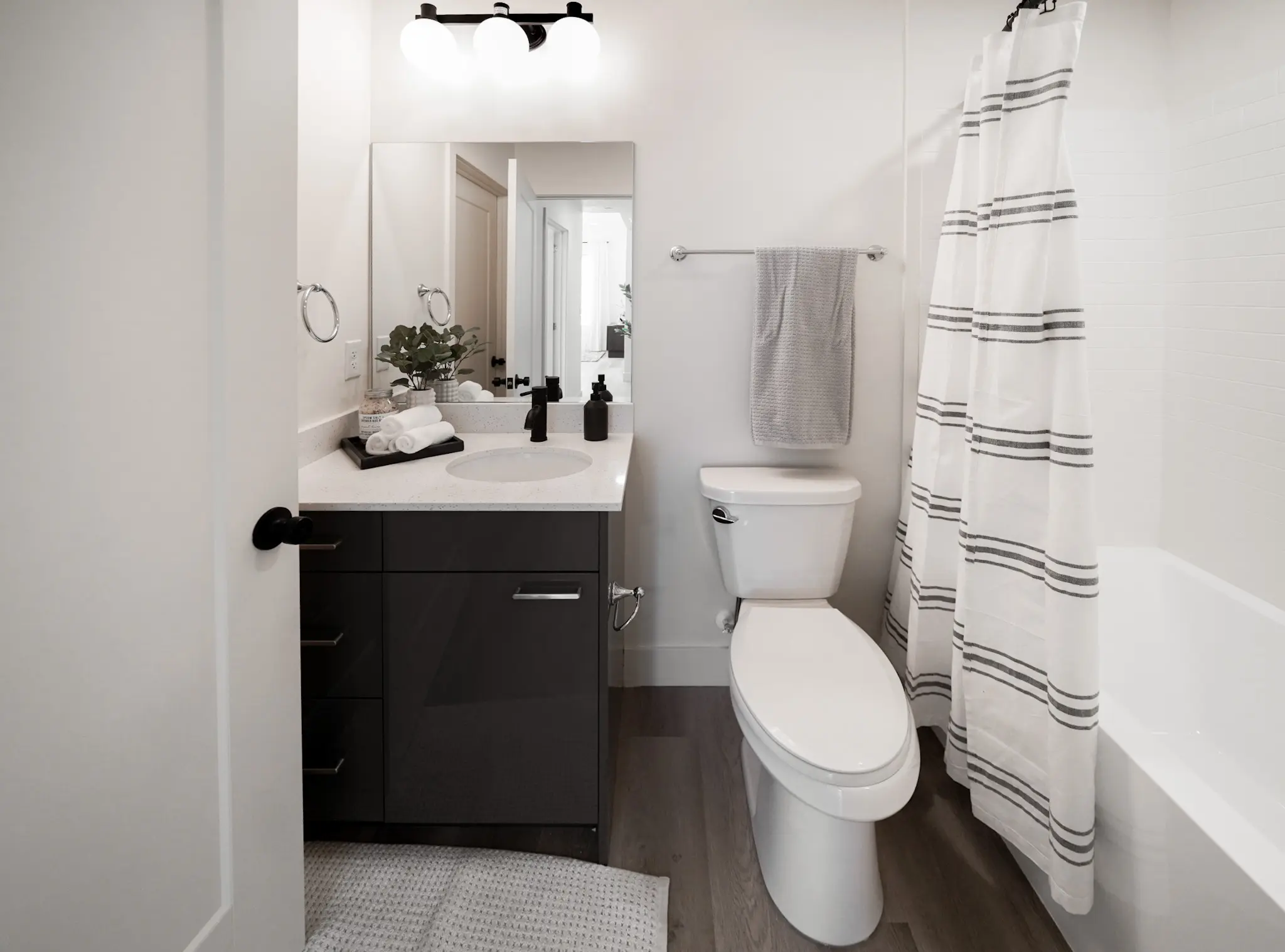 A bathroom the tub has a white shower curtain with black horizontal stripes. The sink cupboard is black.