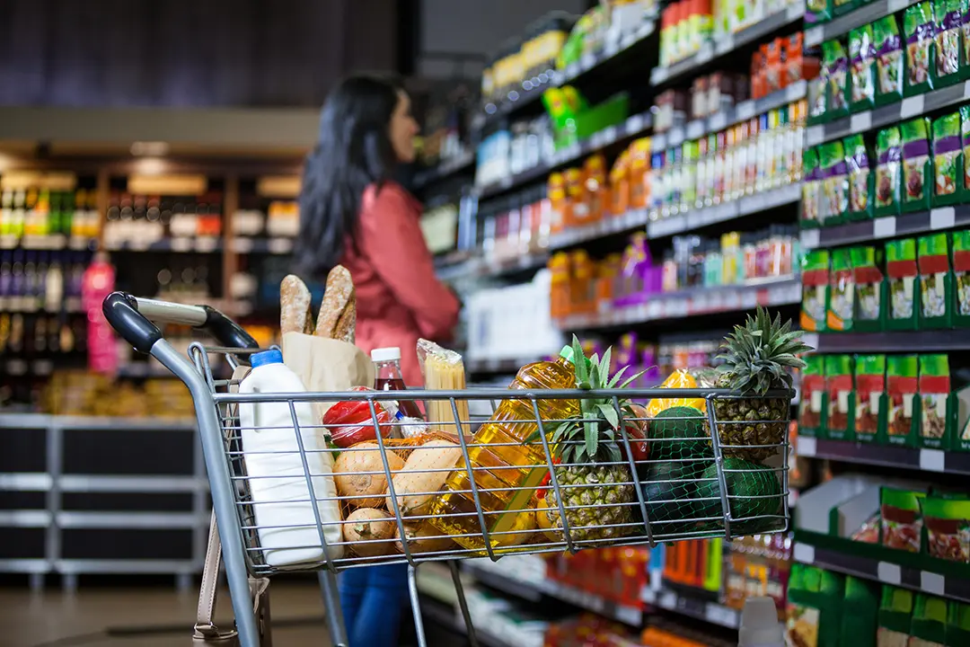 Grocery shopping near The Gallery Apartments, with a full cart of fresh food and a shopper browsing store shelves.