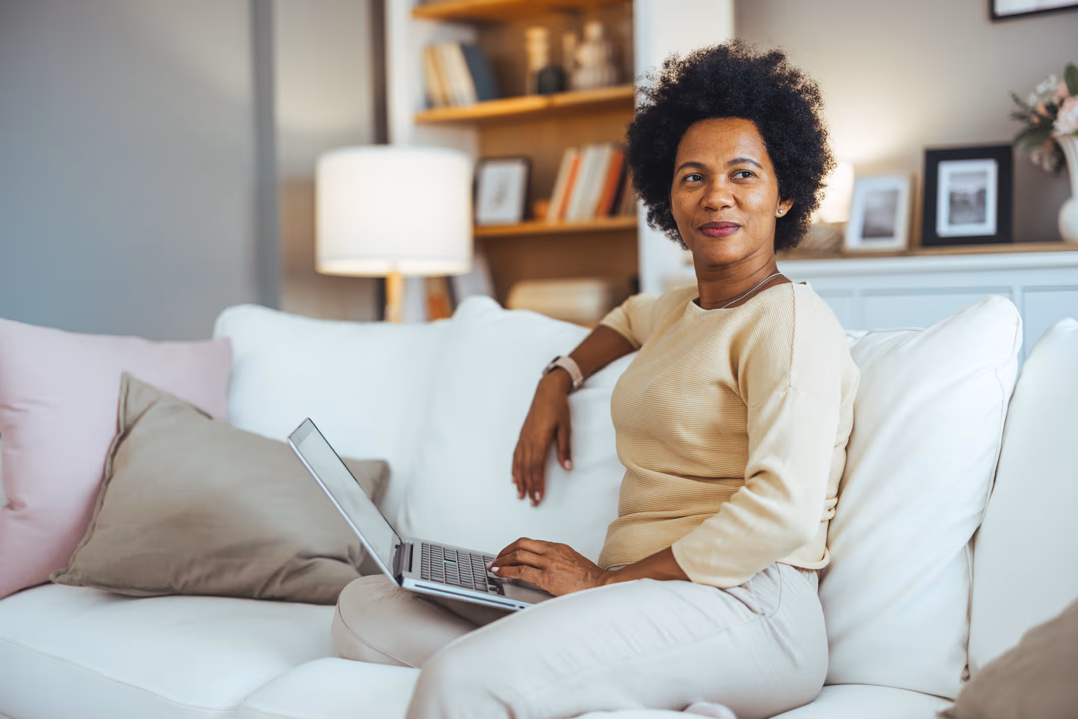 Relaxed woman smiling on a couch with a laptop, reflecting relief from menopausal symptoms with HRT