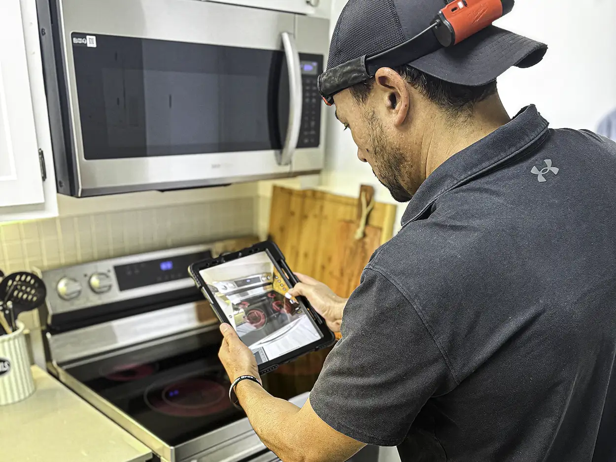 Technician using a tablet to inspect a kitchen stove and microwave.