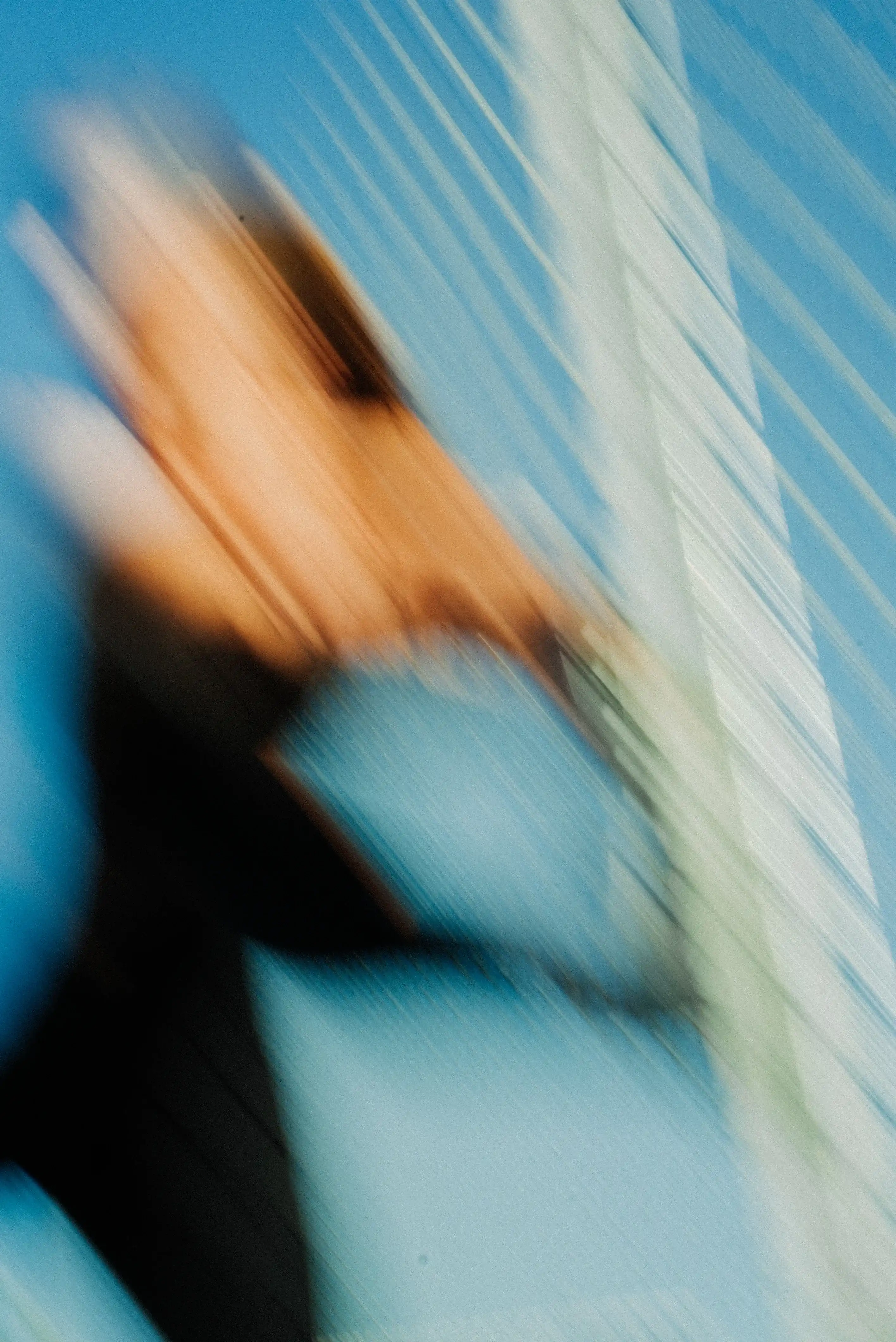 Abstract motion blur of a person with hands near their face against a blue sky and a structure with vertical lines.