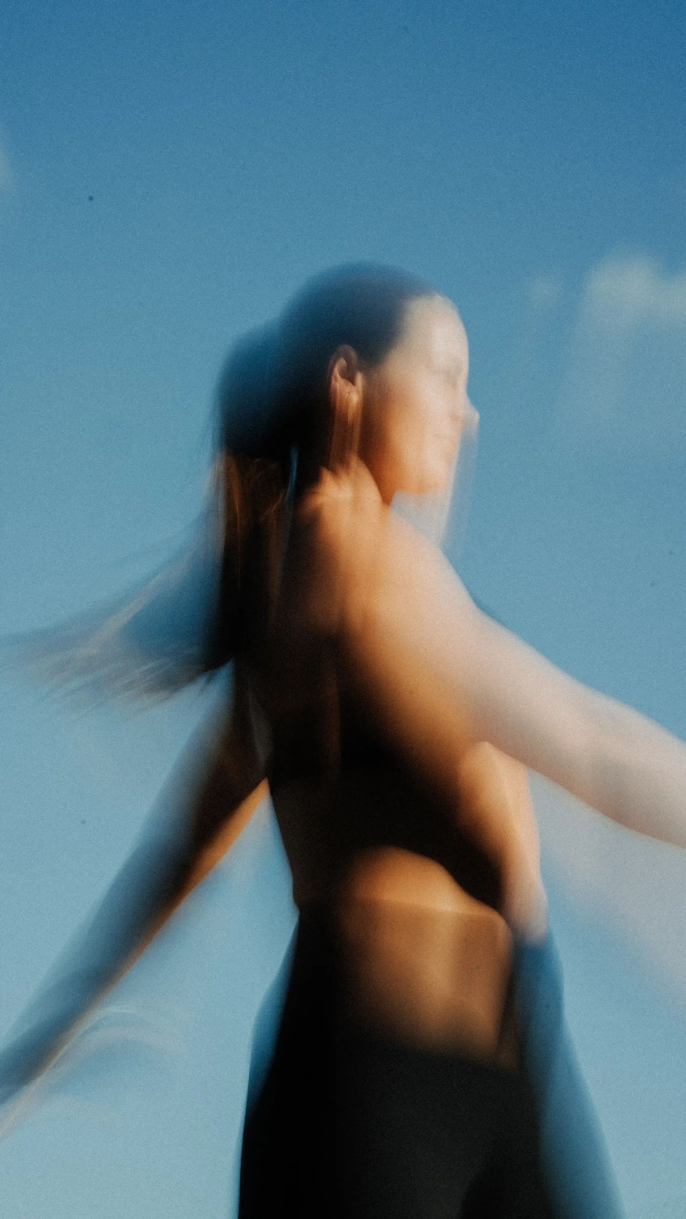 Blurred image of a person with motion effect against a clear blue sky.