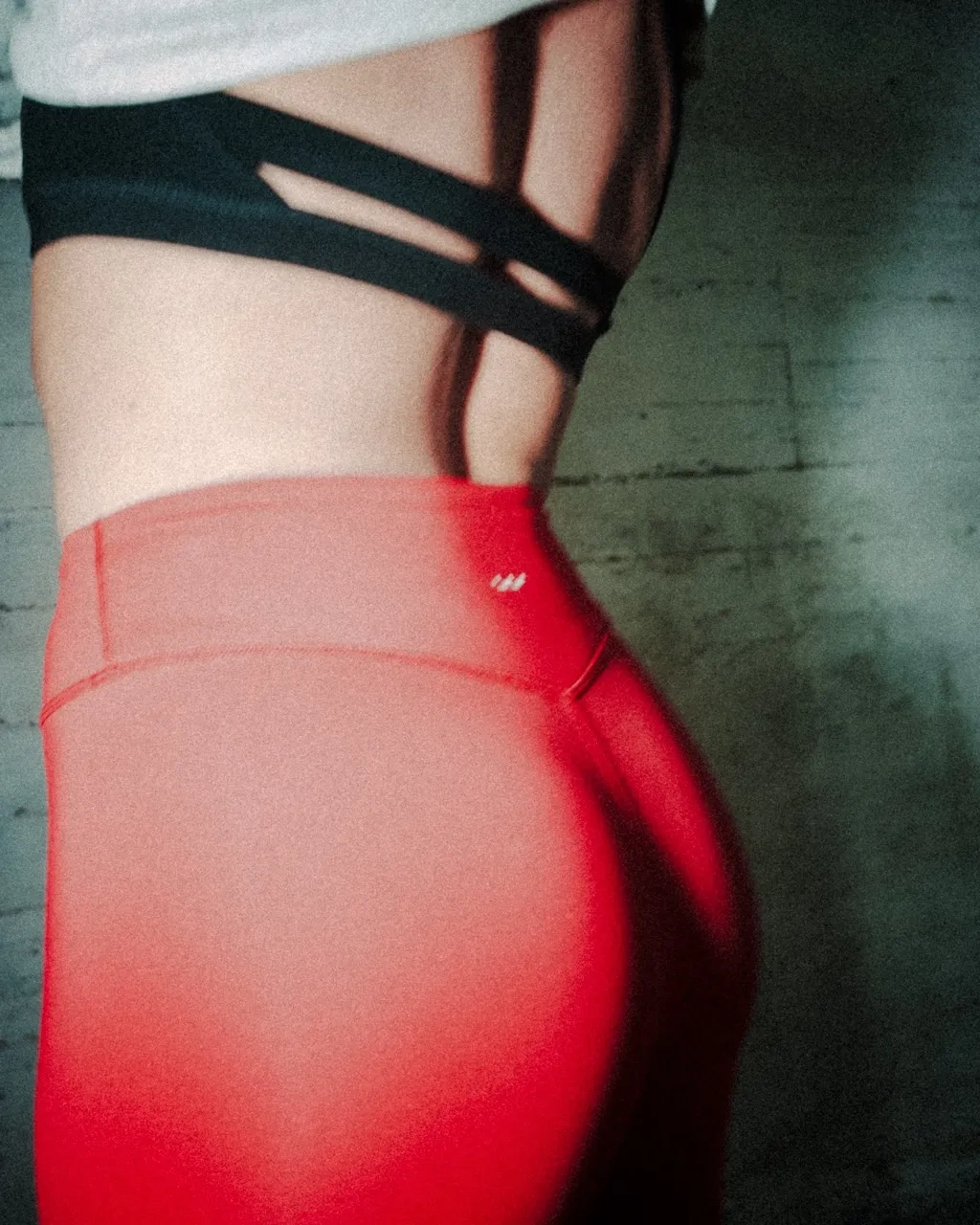 Close-up side view of a person wearing red high-waisted leggings and a black sports bra with crisscross straps.