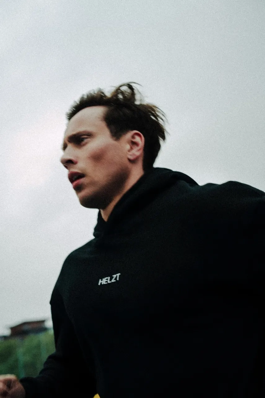 Man running outdoors wearing a black hoodie with the word HELZT on it.