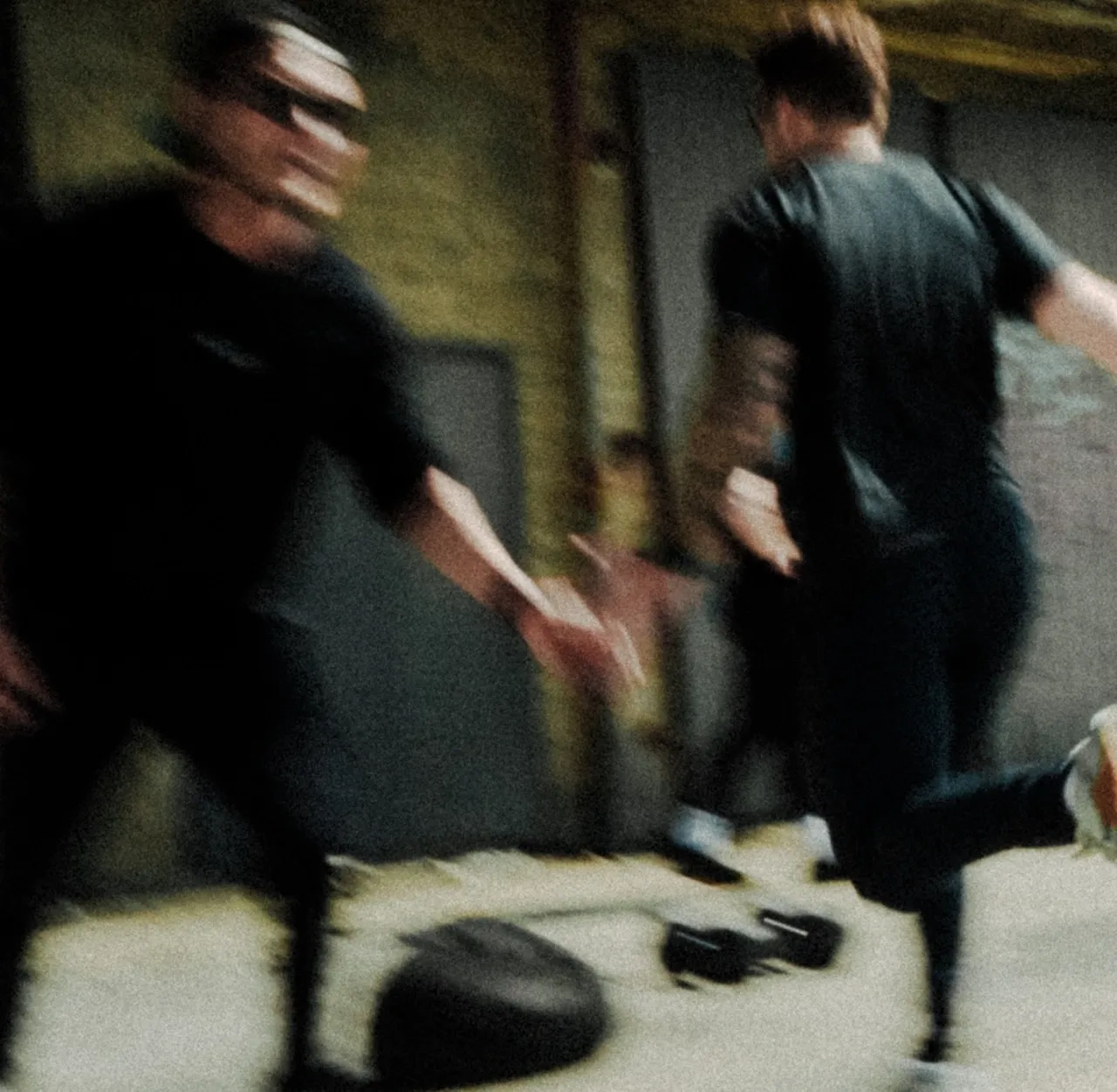 Two people in dark clothing move quickly indoors, creating a blurred effect with one reaching out towards the other.