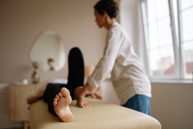 Therapist assisting a person with a leg stretch on a treatment table in a bright room.
