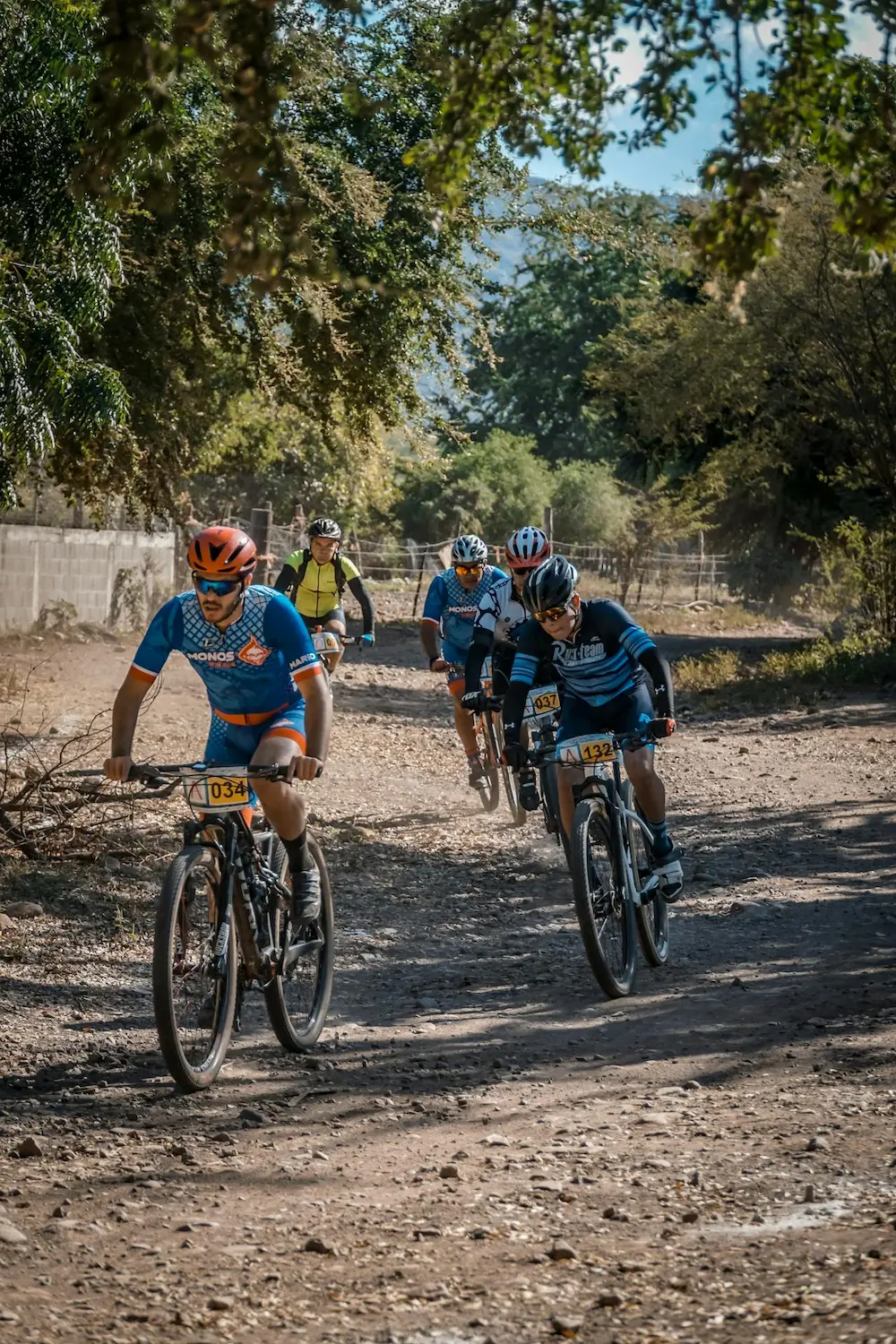 Group of cyclists riding mountain bikes on a rugged dirt trail surrounded by trees.