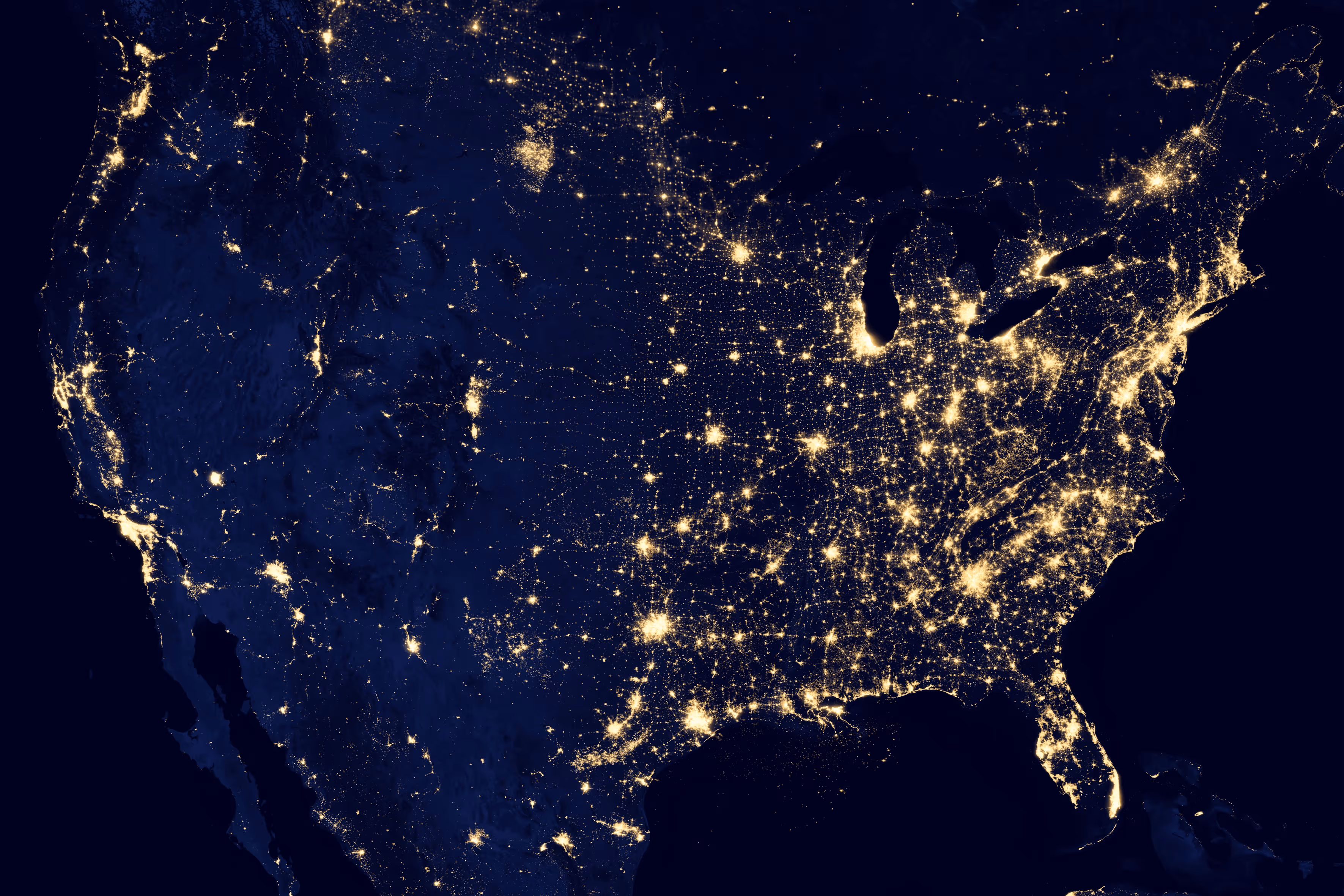 Nighttime satellite view showing city lights across the contiguous United States, highlighting dense urban areas along the East Coast, Midwest, Texas, and California.