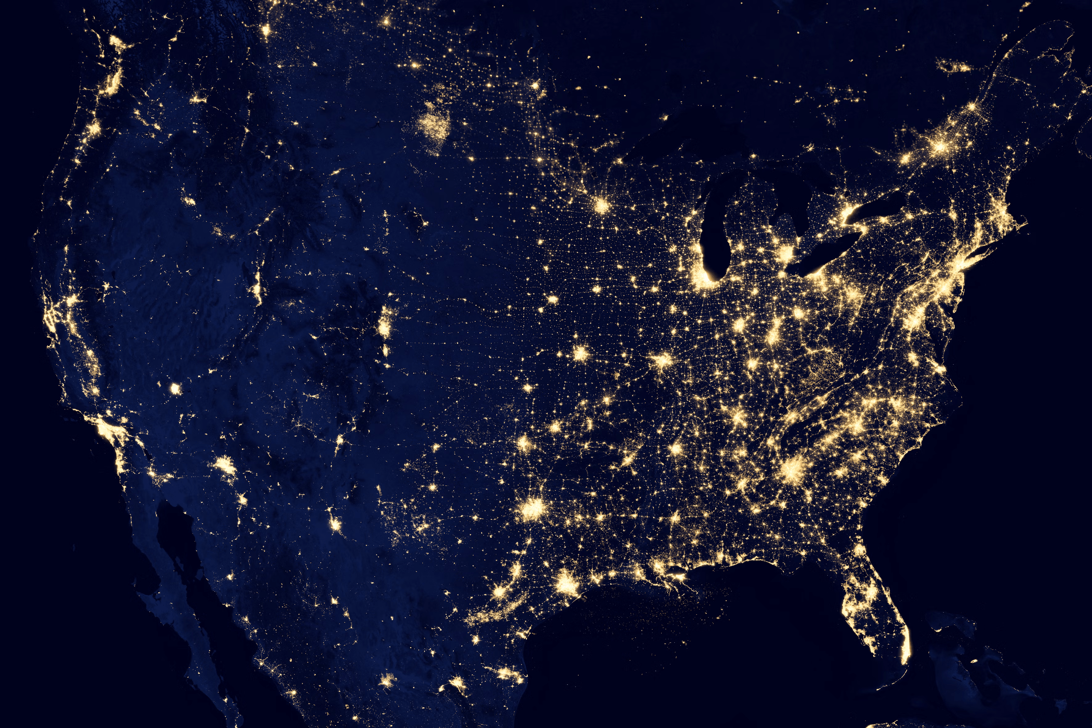Nighttime satellite view showing city lights across the contiguous United States, highlighting dense urban areas along the East Coast, Midwest, Texas, and California.