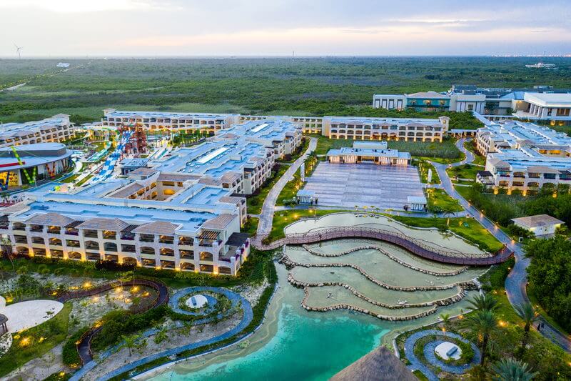 Aerial view of a large resort complex featuring multiple buildings with blue roofs, surrounded by lush greenery.