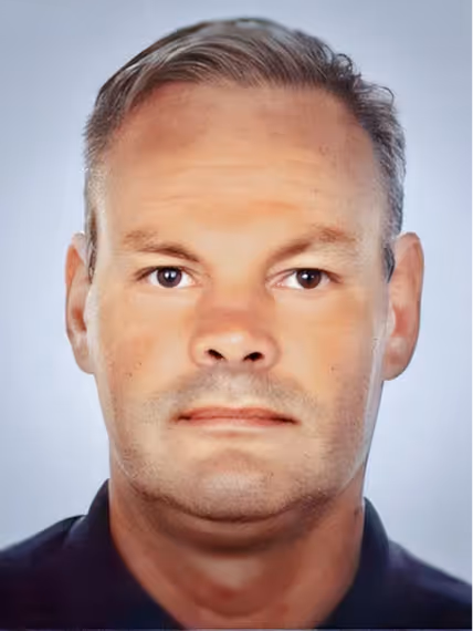 Portrait of a middle-aged man with short grey hair, light skin, and brown eyes, against a light blue background.