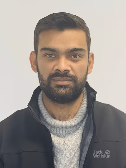 Portrait of a man with short dark hair and beard wearing a grey knit sweater and black Jack Wolfskin jacket.