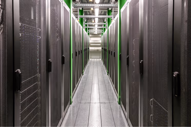 A corridor of server racks inside a data center with gray metal doors and green vertical supports.