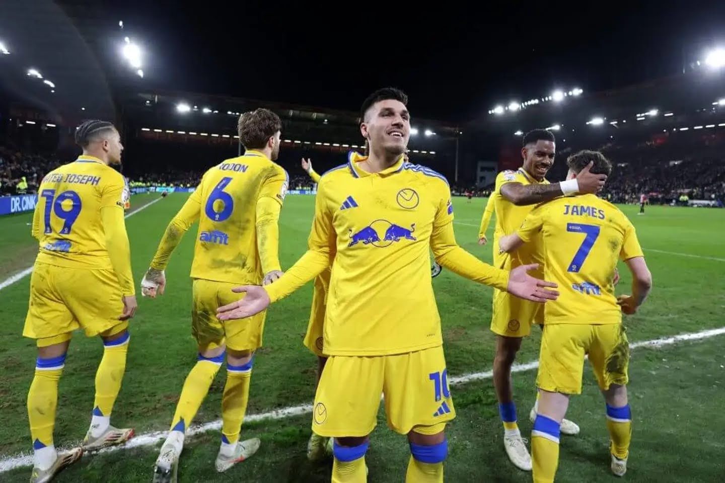 Soccer players in yellow uniforms celebrating on a field under stadium lights at night.