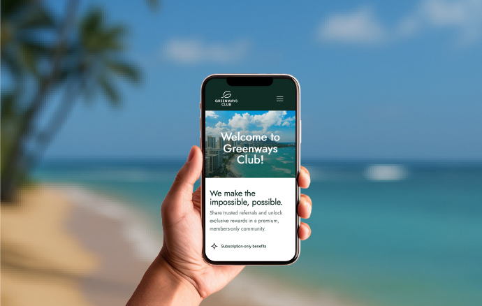 Hand holding a smartphone displaying Greenways Club welcome screen with ocean and beach background.