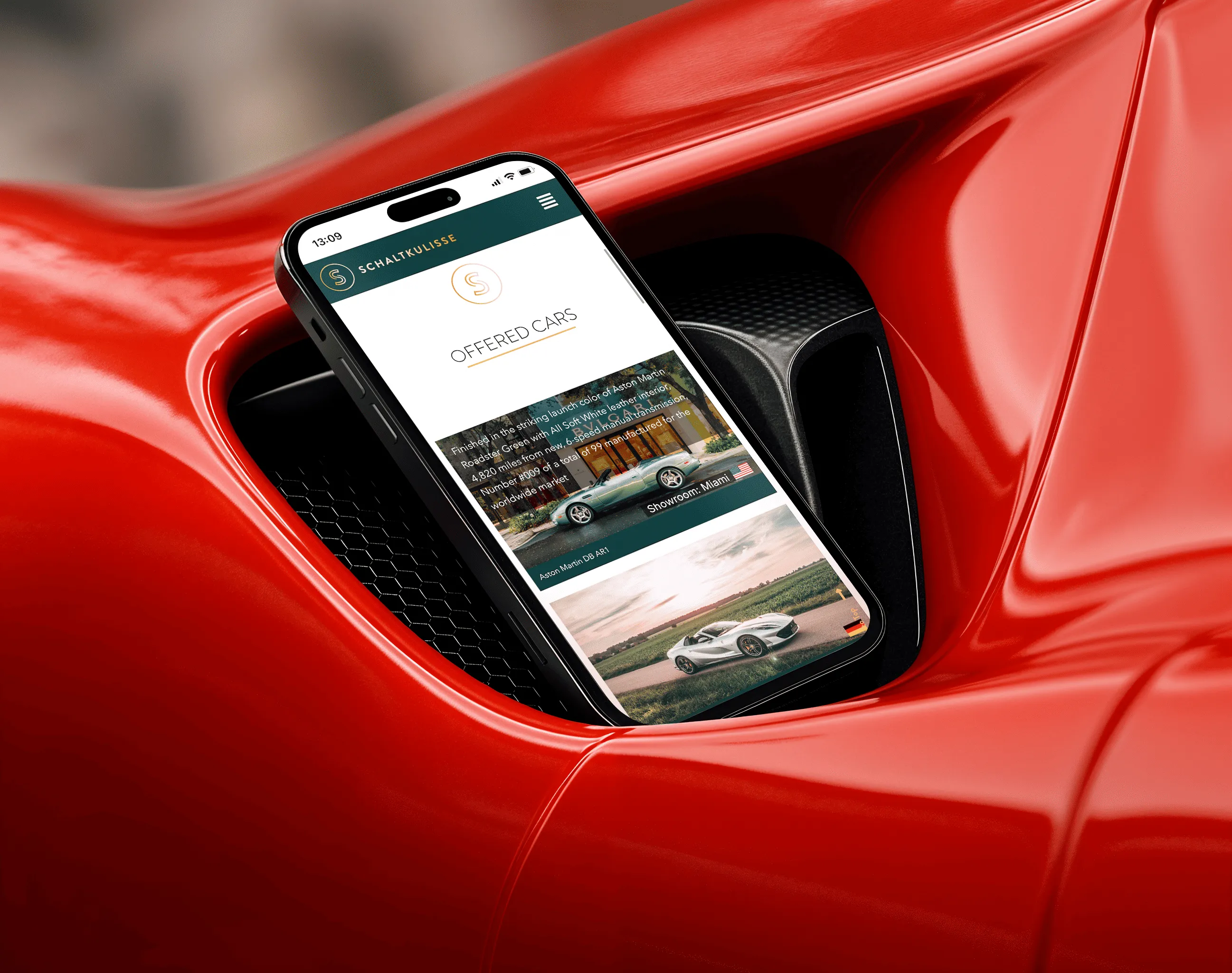 Smartphone displaying a car sales website screen titled 'Offered Cars' resting in the air intake vent of a red sports car.