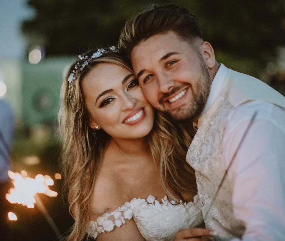 Smiling bride and groom closely embracing outdoors with the bride holding a lit sparkler.