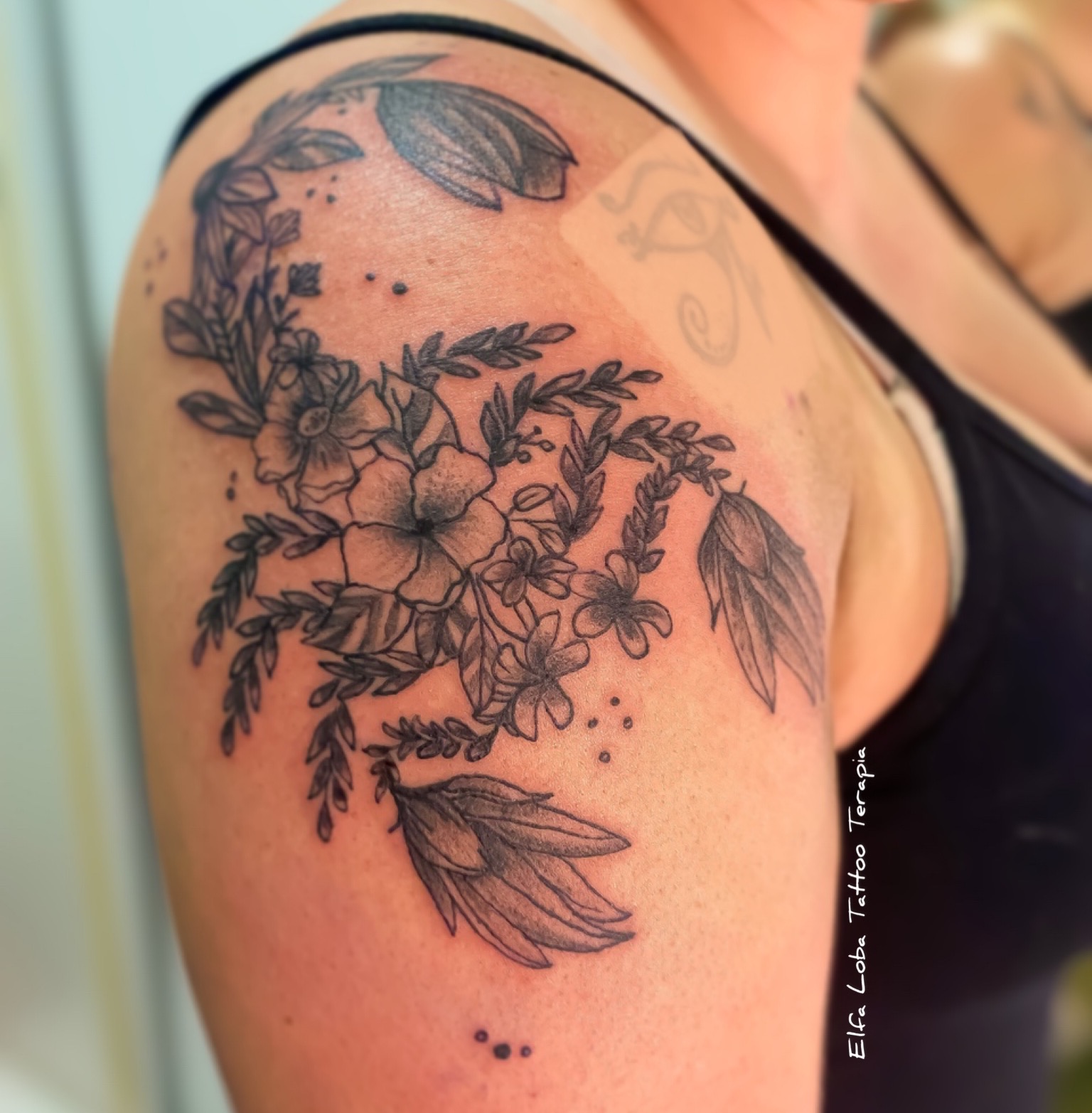 Black and gray floral tattoo with leaves and small flowers on a person's upper arm.