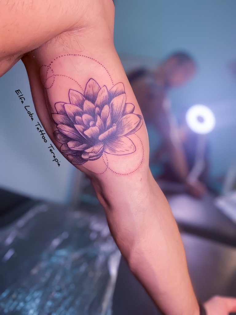 Close-up of a person's arm with a detailed black lotus flower tattoo near the elbow.