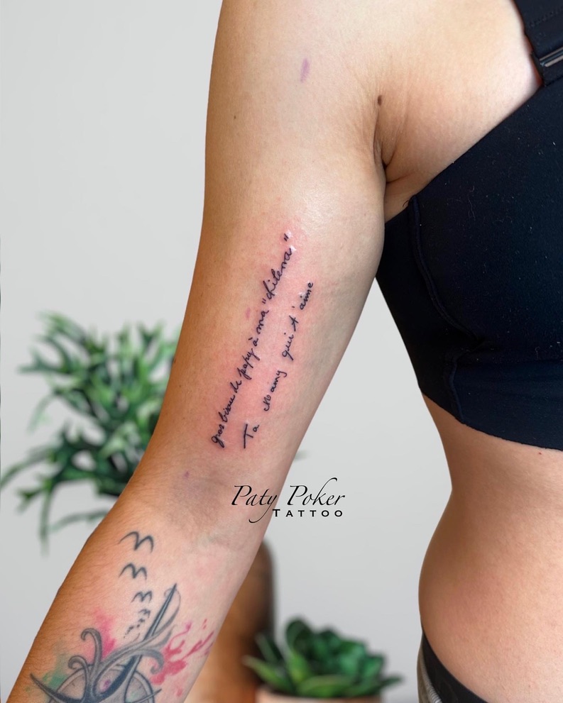 Arm tattoo with French text in cursive script on inner bicep of a person wearing a black top.